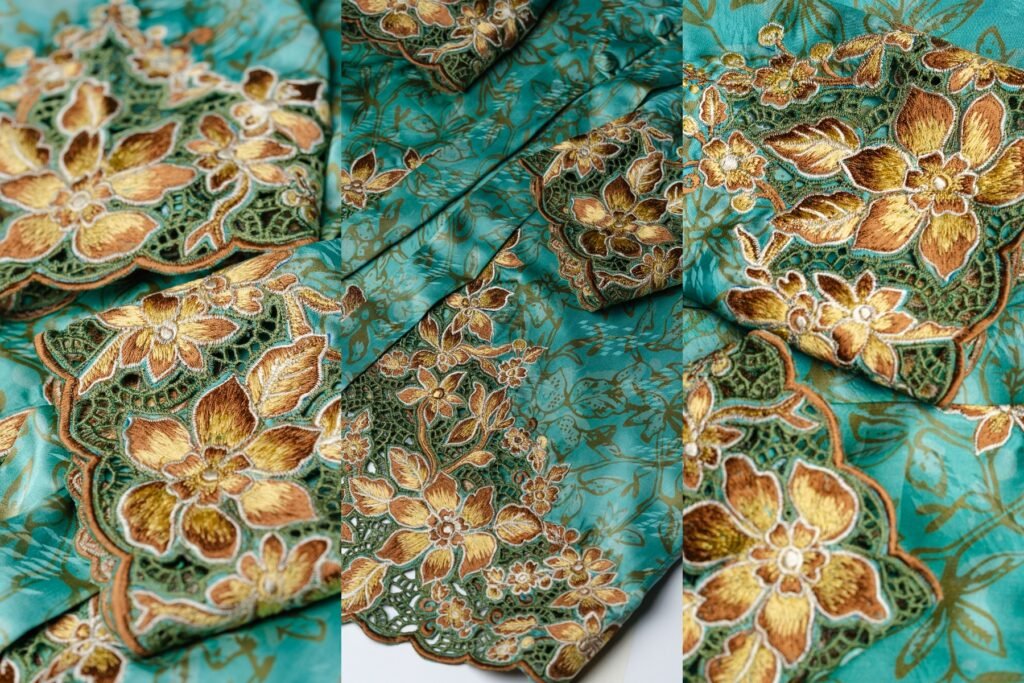 Pada bahagian hujung lengan dan bawah baju, sulaman bunga emas dengan benang berkilau menyerlah di atas dasar hijau, mencipta kontras yang elegan dan berkelas. Warna gelap di bahagian bawah memberi kedalaman serta menonjolkan lagi perincian bunga yang disulam. Apabila dikenakan di bawah cahaya, sulaman benang emas ini memantulkan kilauan lembut, seolah-olah menyinari setiap langkah pemakai. Gabungan warna ini bukan sahaja melambangkan kemewahan, tetapi juga keharmonian antara unsur alam dan budaya — menjadikan rekaan ini lambang keindahan tradisi yang terus hidup dalam sentuhan moden Kechubung Butik.